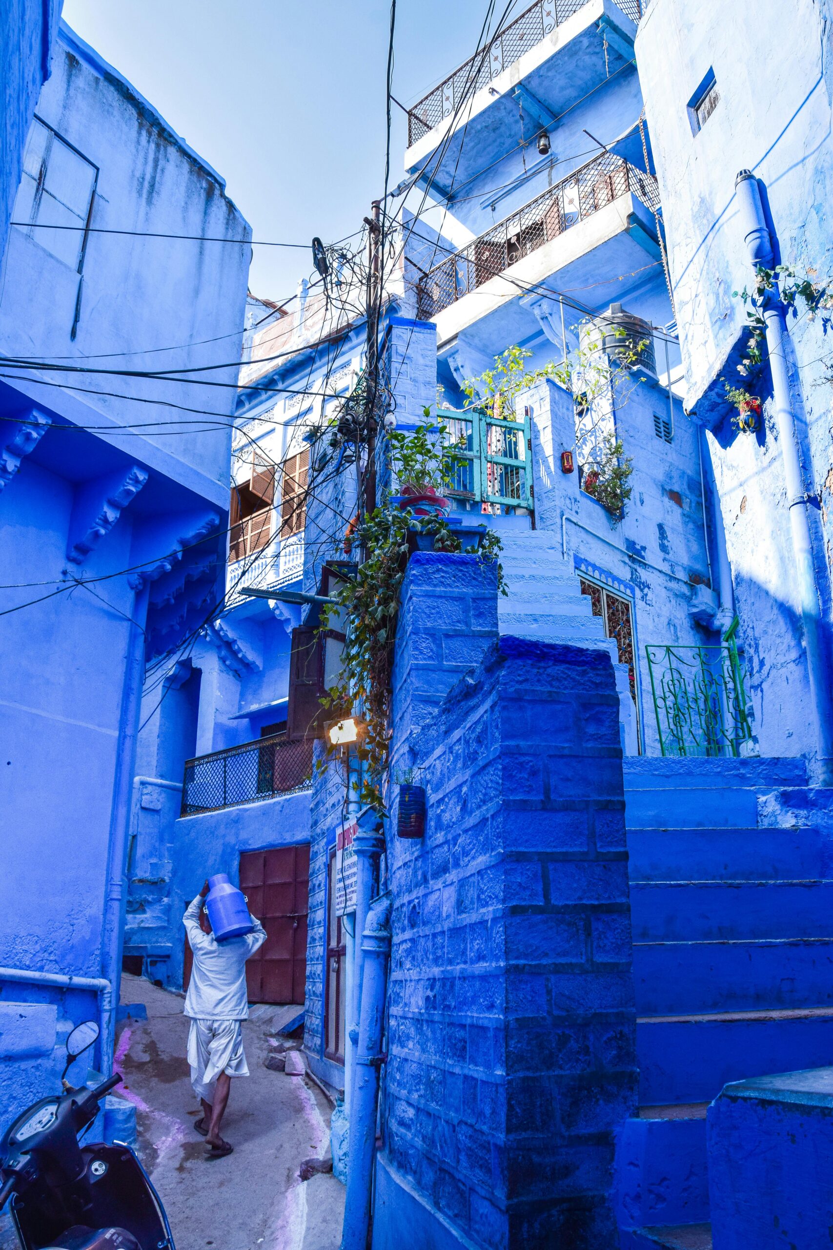 A man walks through a vibrant blue alley in Jodhpur, India, showcasing iconic architecture.